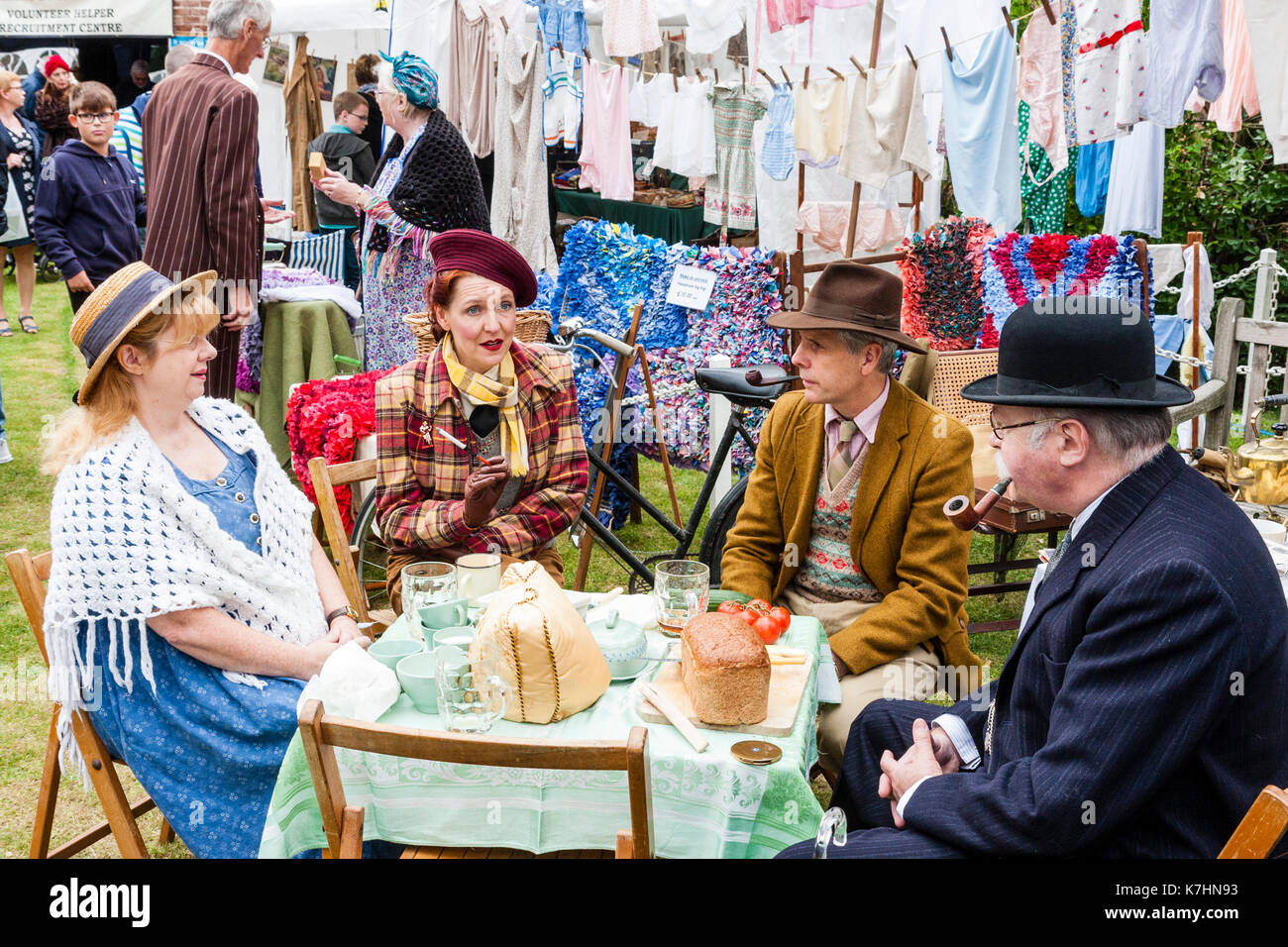 Two mature couples dressed in upper class clothing circa 1940's re-enacting a world war two picnic at a table with washing hanging behind them. Salute to the 40's weekend at Chatham Historic Dockyard. Elderly man smoking a pipe. Stock Photo