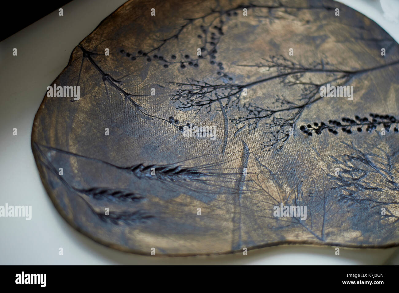 Dark brown dish made of clay, uneven shape with the imprint of grass
