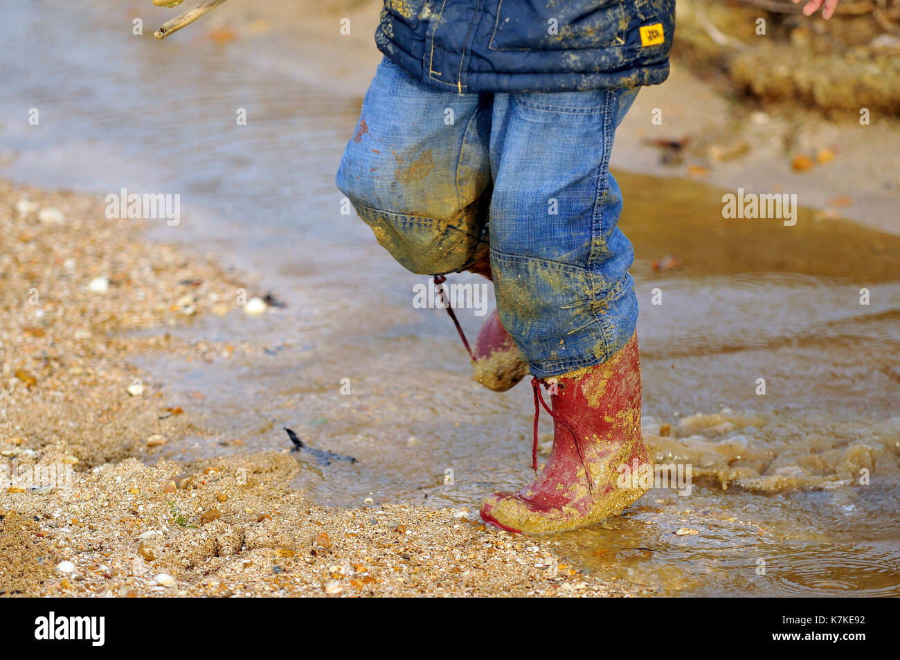 A child or kid wearing red wellies wellington boots and covered in mud and  water wet through jumping in puddles in the rain and wet weather in winter  Stock Photo - Alamy