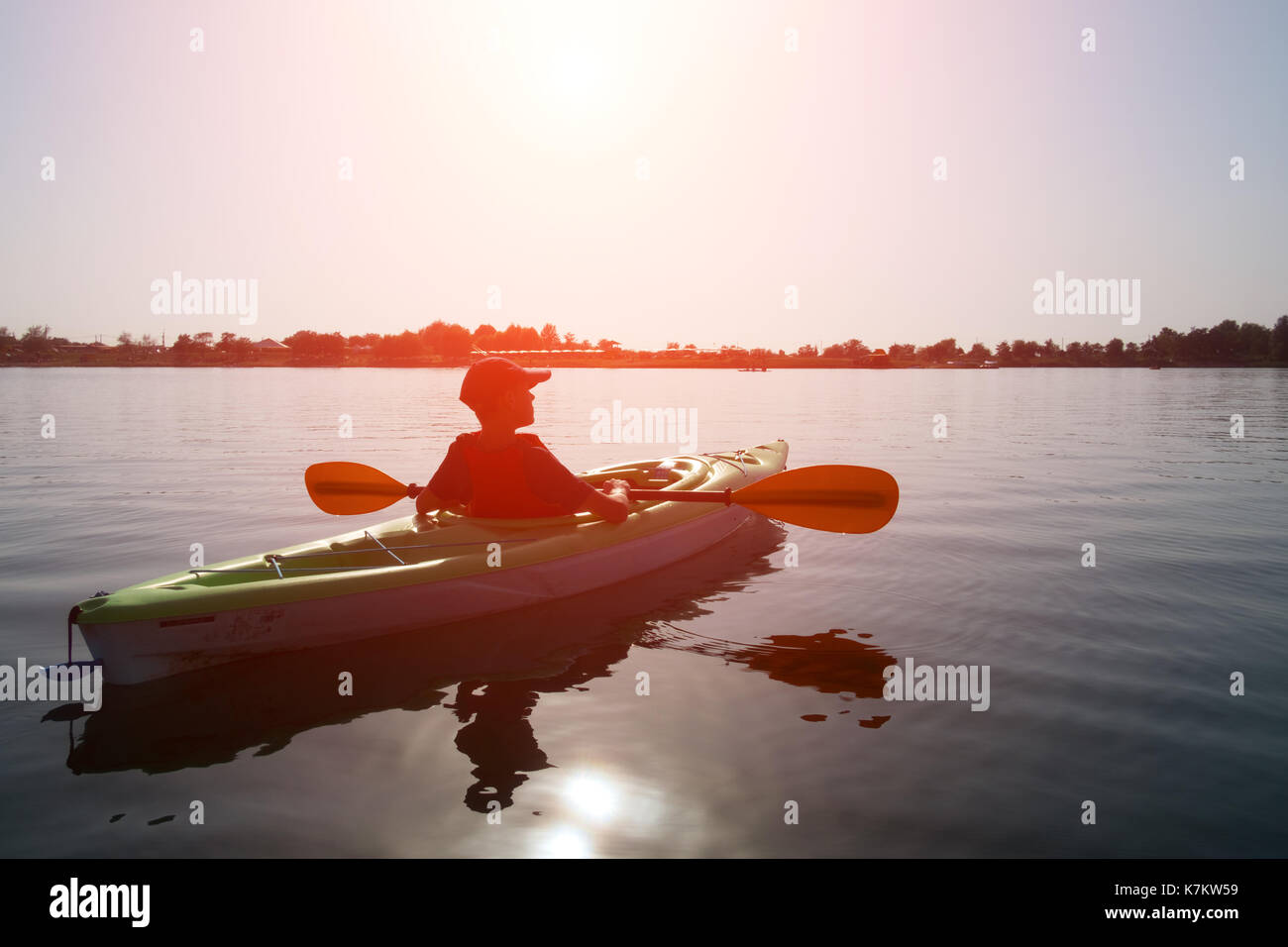 Boy in life jacket on green kayak. Sunny day on wonderful lake. Summer
