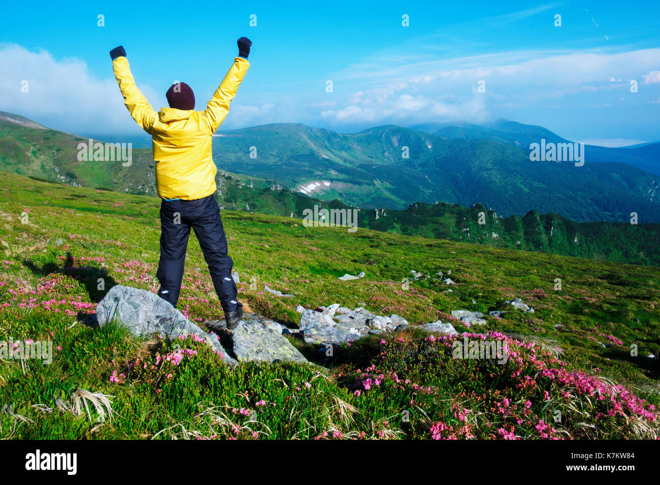Alone tourist in yellow jacket with hands up on high mountains. Stock Photo