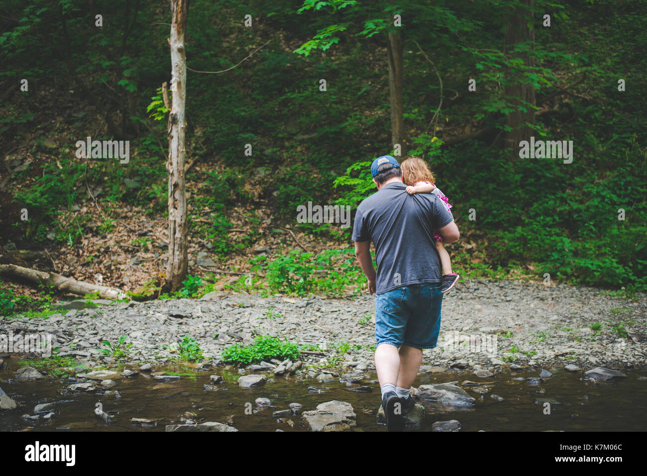 A father carries his daughter during a hike in the woods. Stock Photo