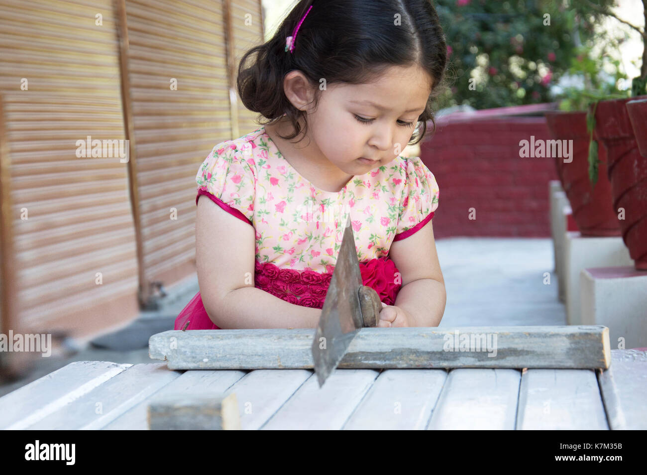 Little girl carpenter sawing wood plank with a handsaw outdoors. Indian, Asian. Stock Photo