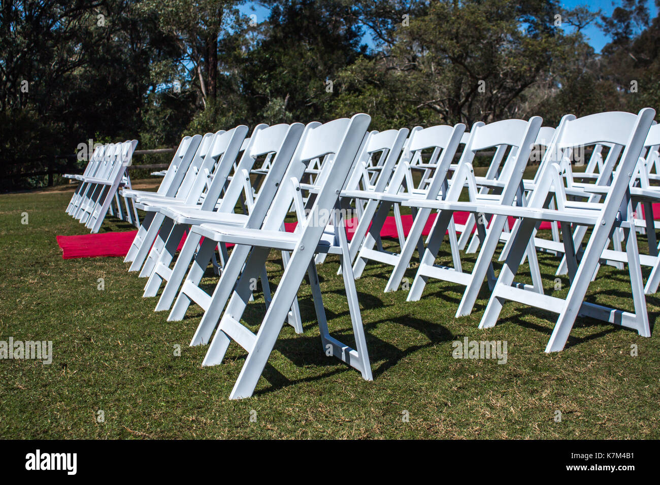 White ceremony chairs set up outdoors with red carpet aisle on green