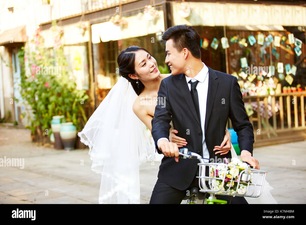 romantic asian newly wed couple having fun riding a bicycle together. Stock Photo