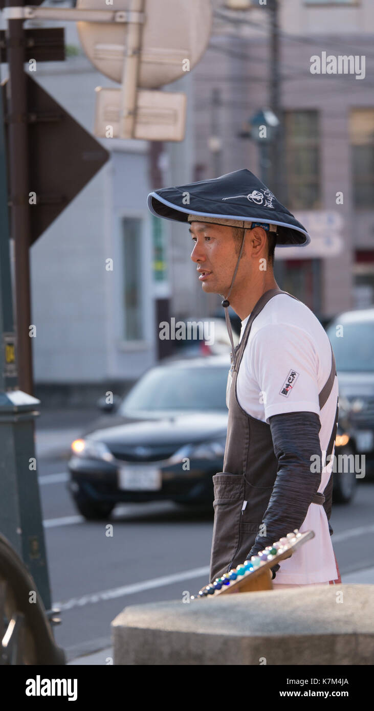 Young Japanese man working as a tourist rickshaw driver in Otaru, Japan.  Profile shot showing black straw hat, white shirt and black arm coverings. Stock Photo