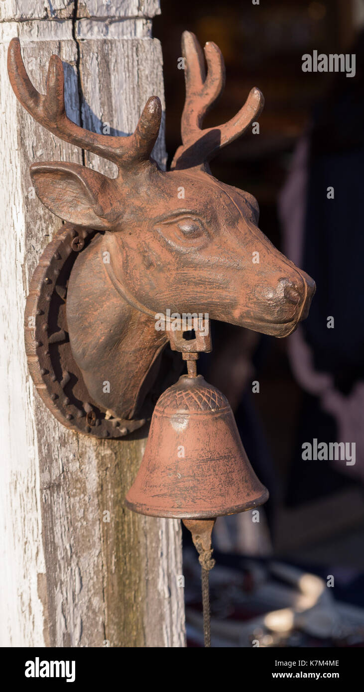 Rusted, metal deer head with antlers and bell around neck door bell.  Afternoon sun creating warm light profile and wooden post and black background. Stock Photo