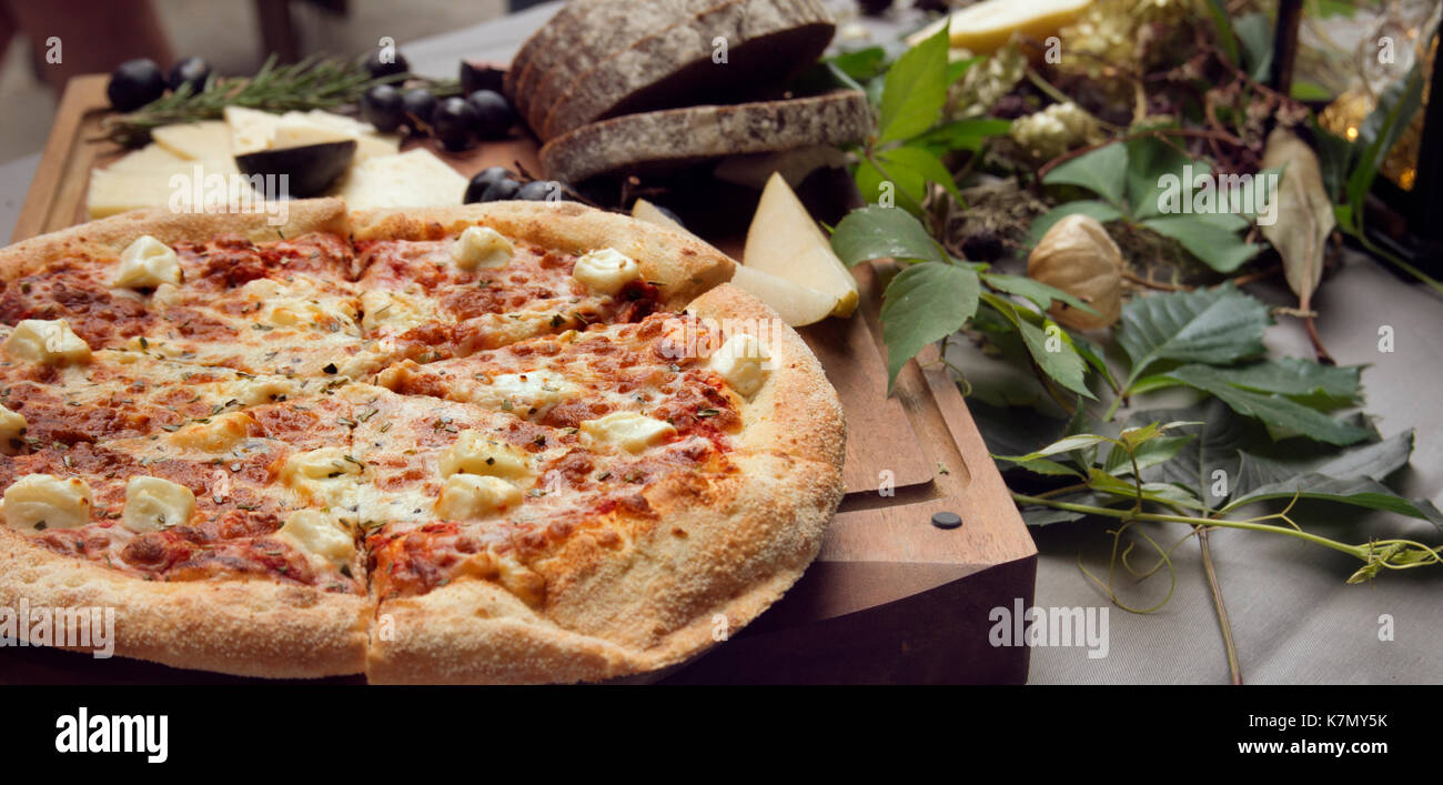 Pizza on board, cheese and leafs on the table Stock Photo