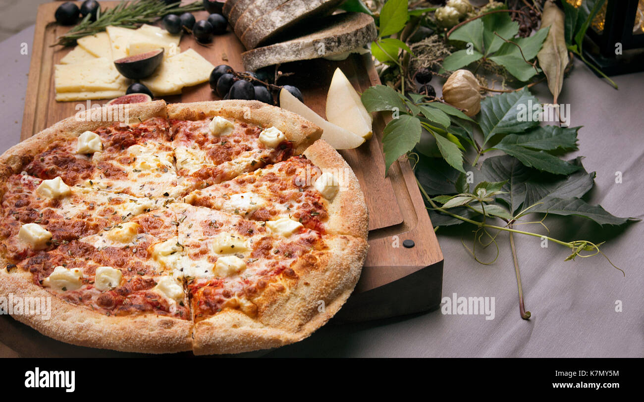Pizza on board, cheese and leafs on the table Stock Photo