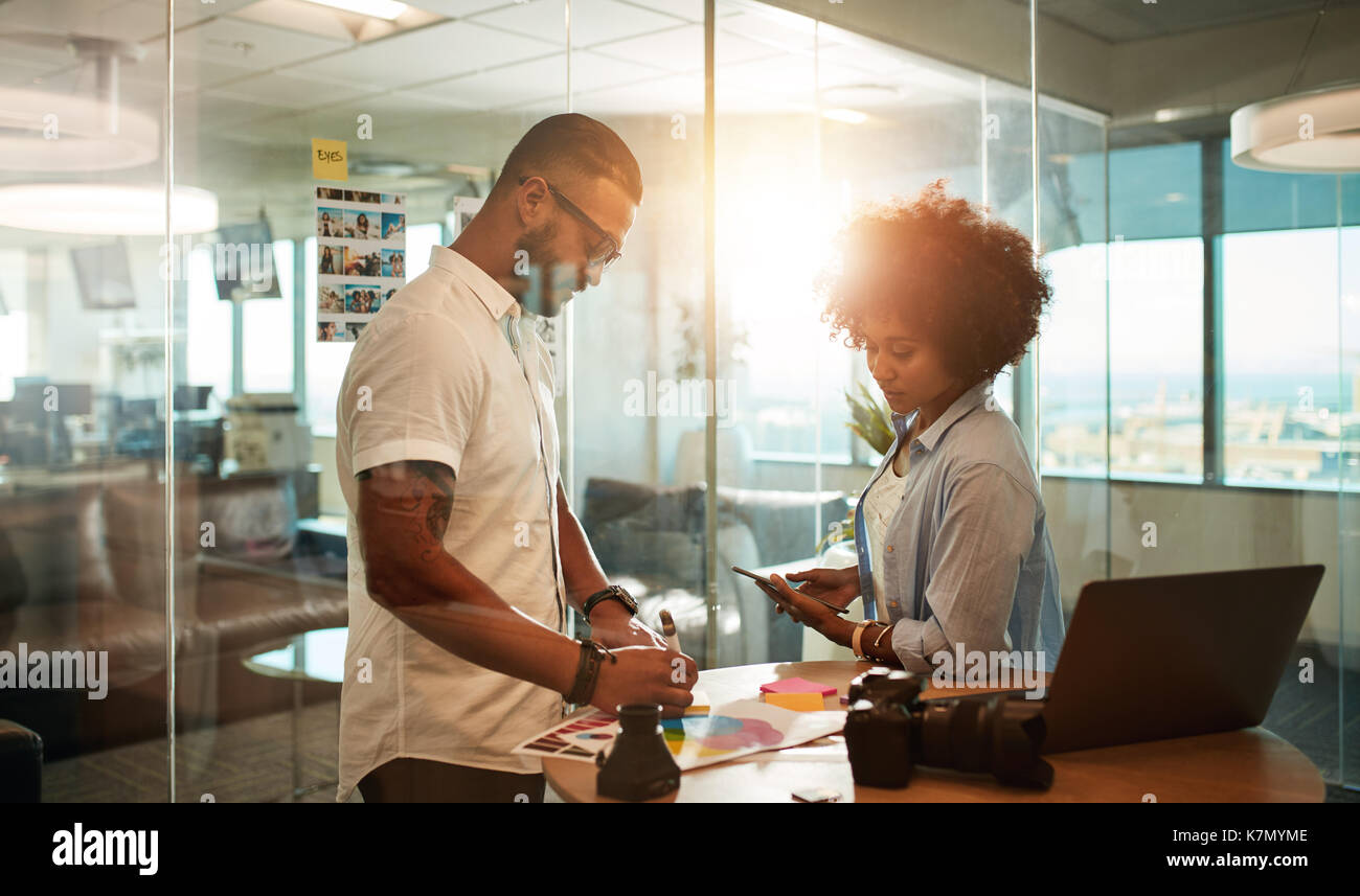 Two young photographers discussing shooting plan at creative workplace. Design professionals working together in modern office. Stock Photo