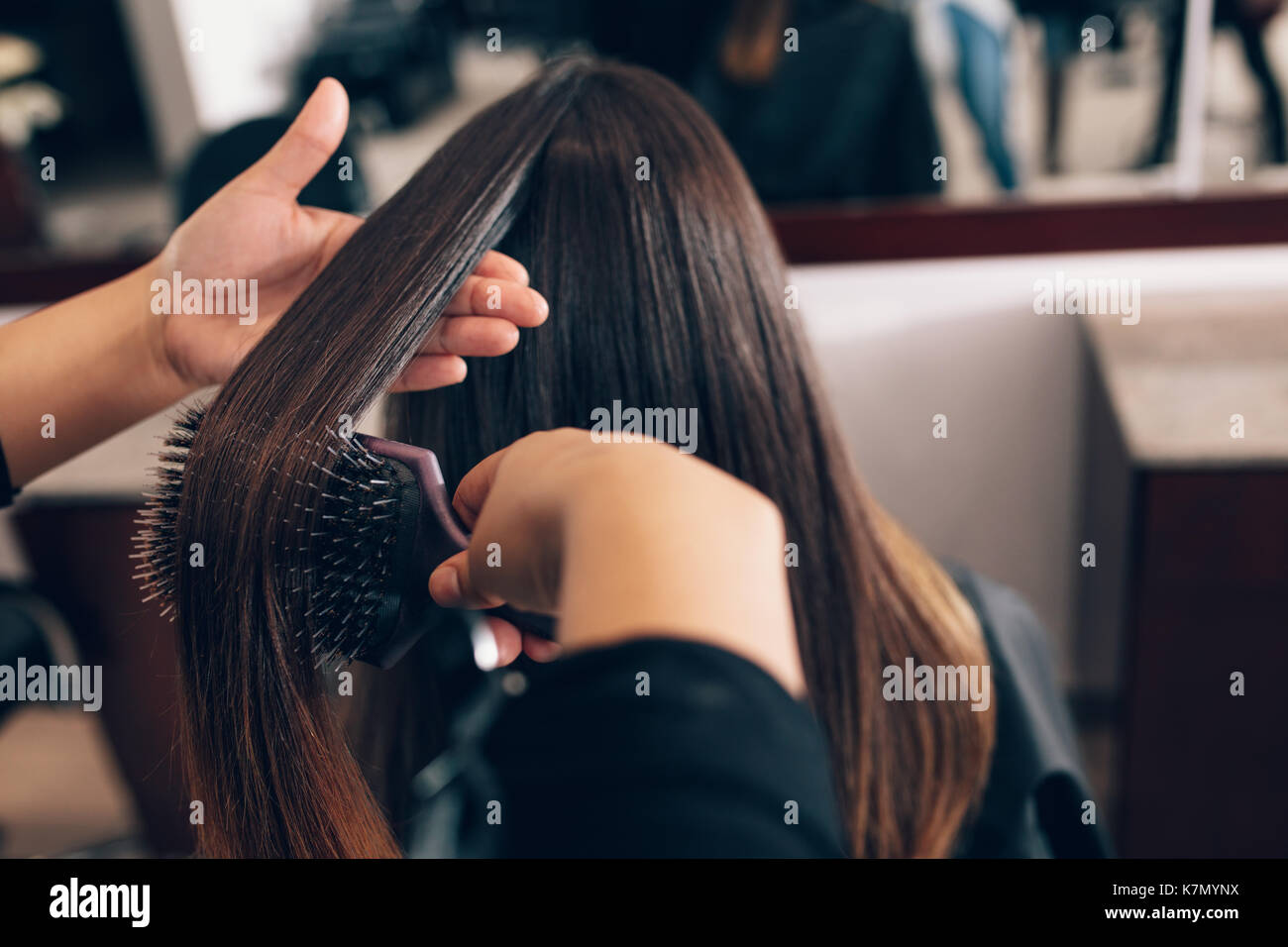 Professional hairdresser styling the hair of a customer at salon. Female hair stylist combing hair using a hair brush. Stock Photo