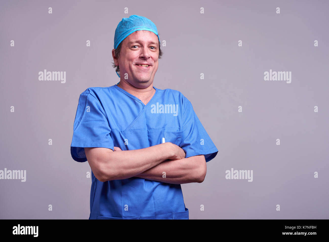 A happy middle aged male doctor standing in blue scrubs and laughing Stock Photo