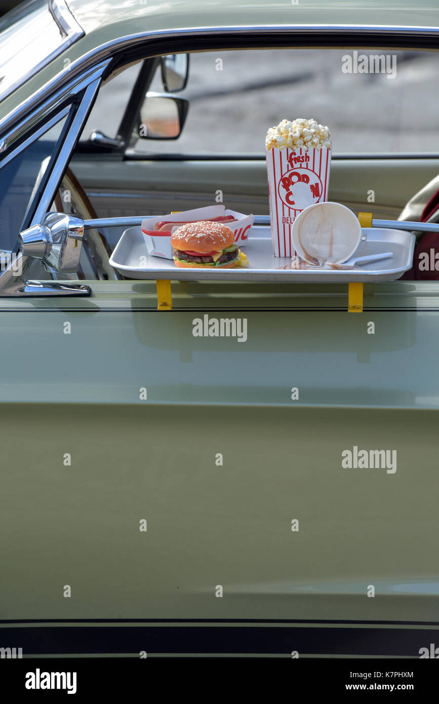 A beef burger and chips on the door of a classic American car in a drive through takeaway or drive in cinema with popcorn. Fast foods restaurants Stock Photo