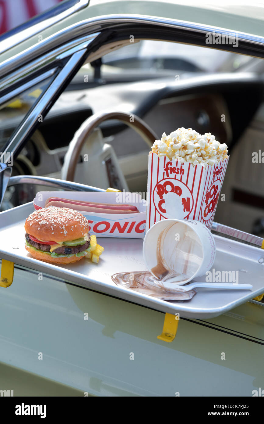 A beef burger and chips on the door of a classic American car in a drive through takeaway or drive in cinema with popcorn. Fast foods restaurants Stock Photo