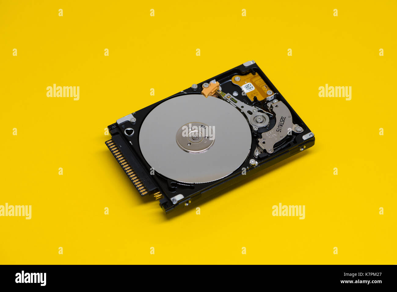 Close-up of an opened computer hard drive disk on yellow colored background. Read-write head retracted. Stock Photo