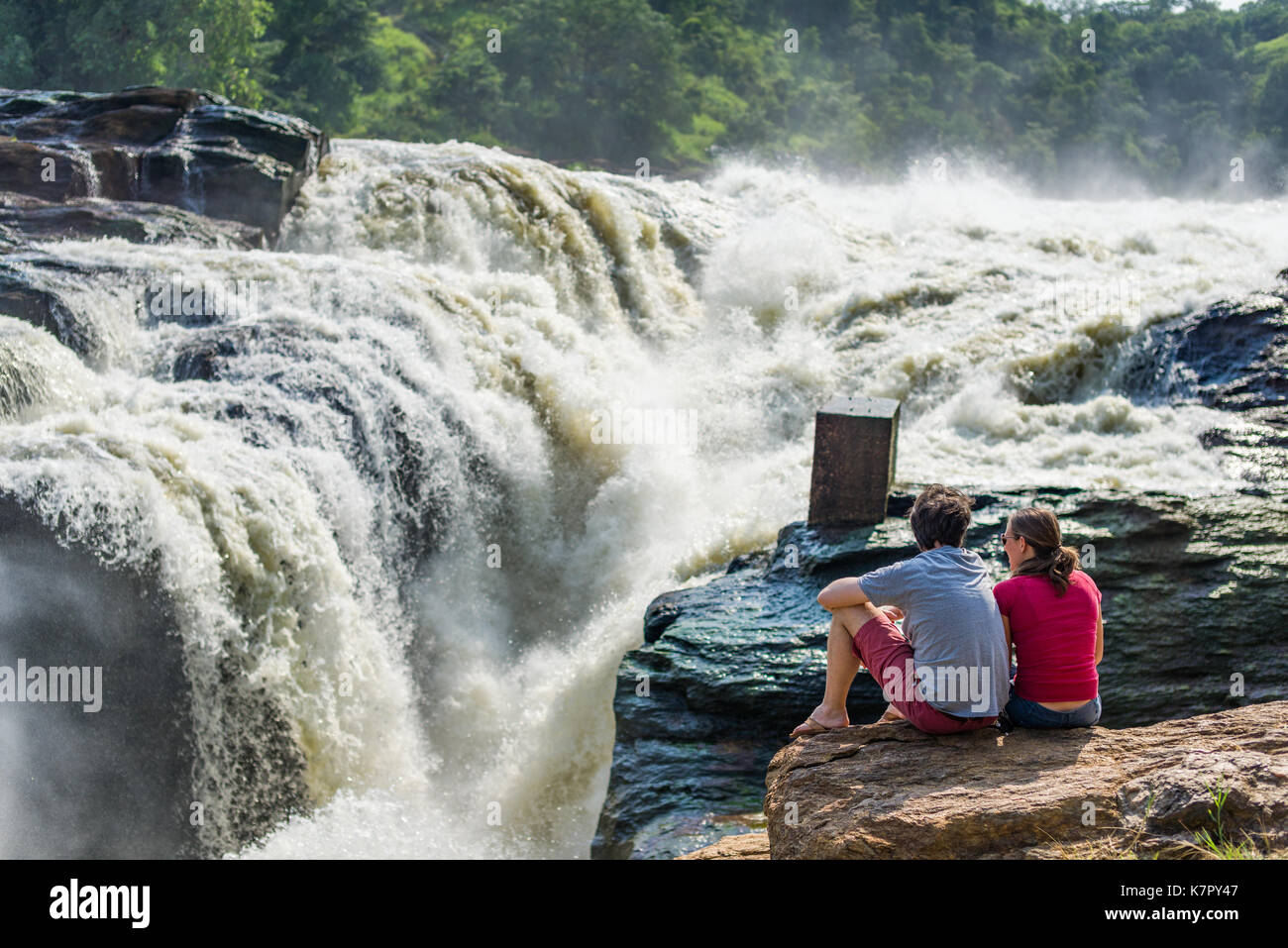 A couple sit on the rock edge viewing the river flowing towards Murchison Falls, Uganda Stock Photo