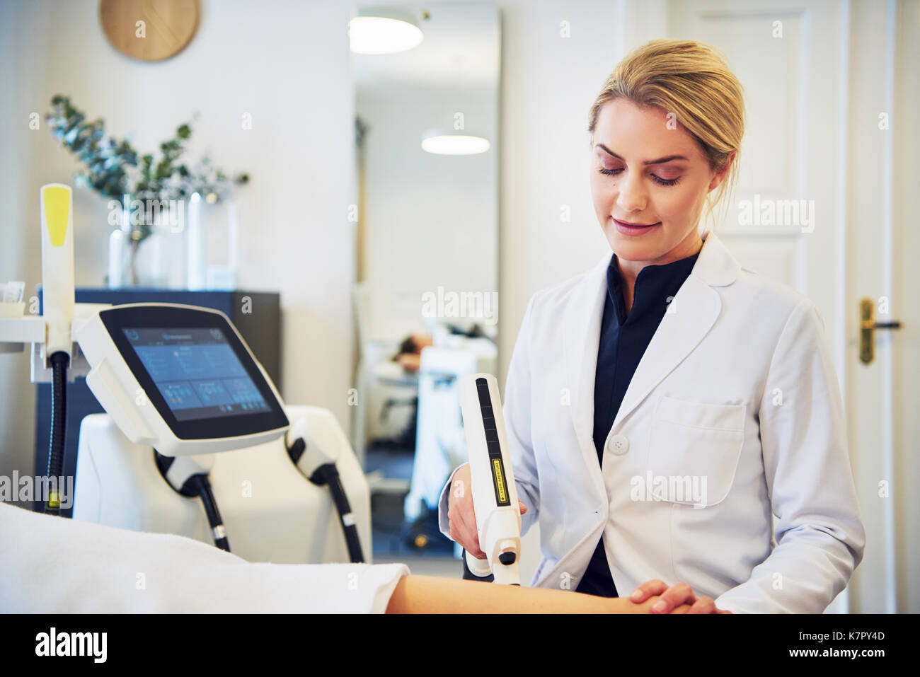 Focused young female beautician performing electrolysis on the legs of a woman lying on a table in a beauty clinic Stock Photo