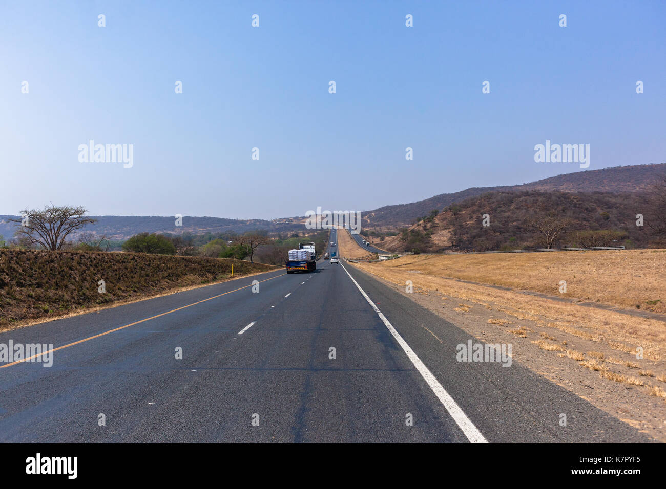Drivers View travelling road highway with vehicles route through surrounding dry hills countryside landscape Stock Photo