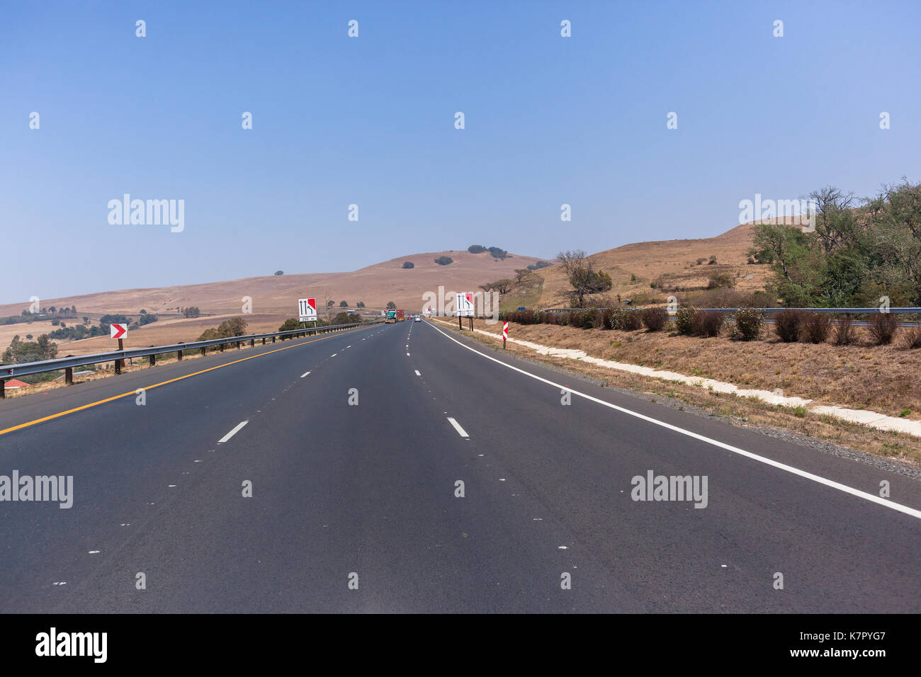 Drivers View travelling road highway with vehicles route through surrounding dry hills countryside landscape Stock Photo