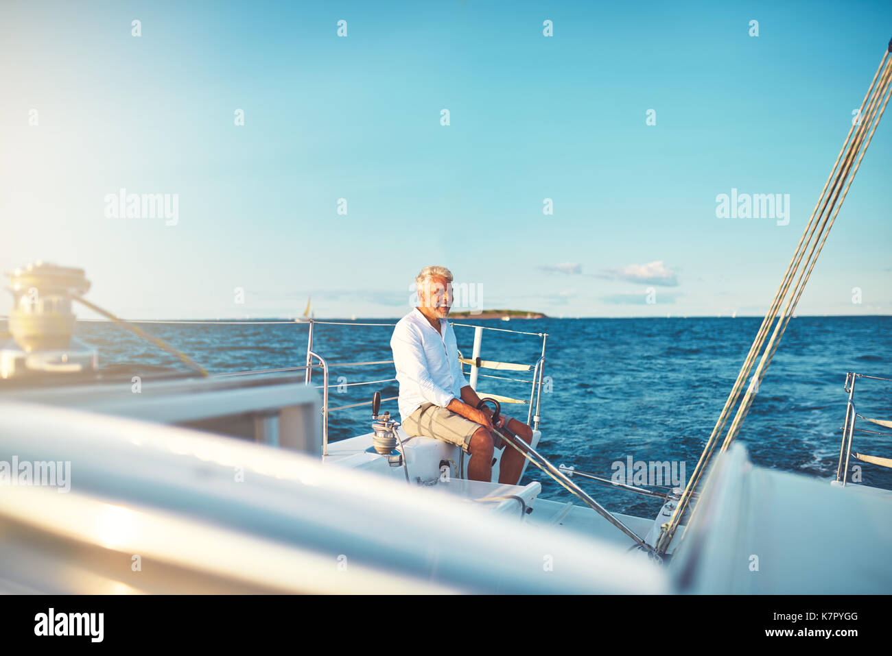 Smiling mature man sitting on the deck of his boat while sailing along ...