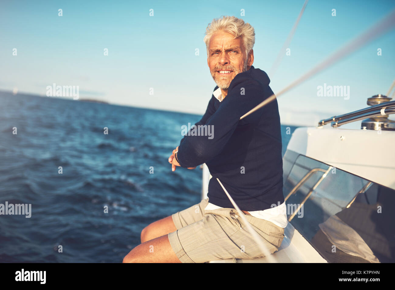 Smiling mature man sitting and leaning on the railing of his boat deck ...