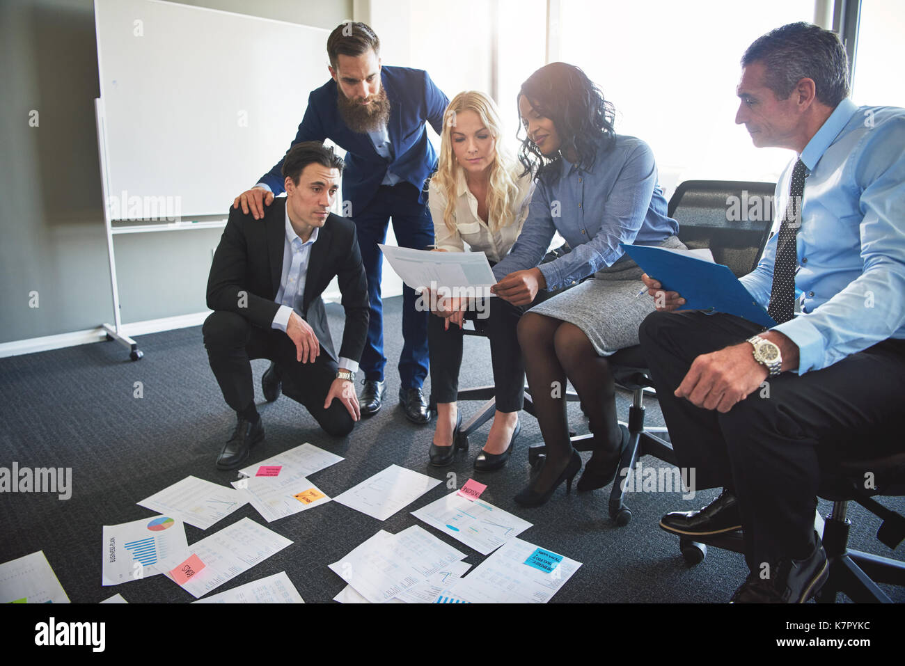 Group of diverse businesspeople brainstorming together with files laid out on the floor while working in a modern office Stock Photo