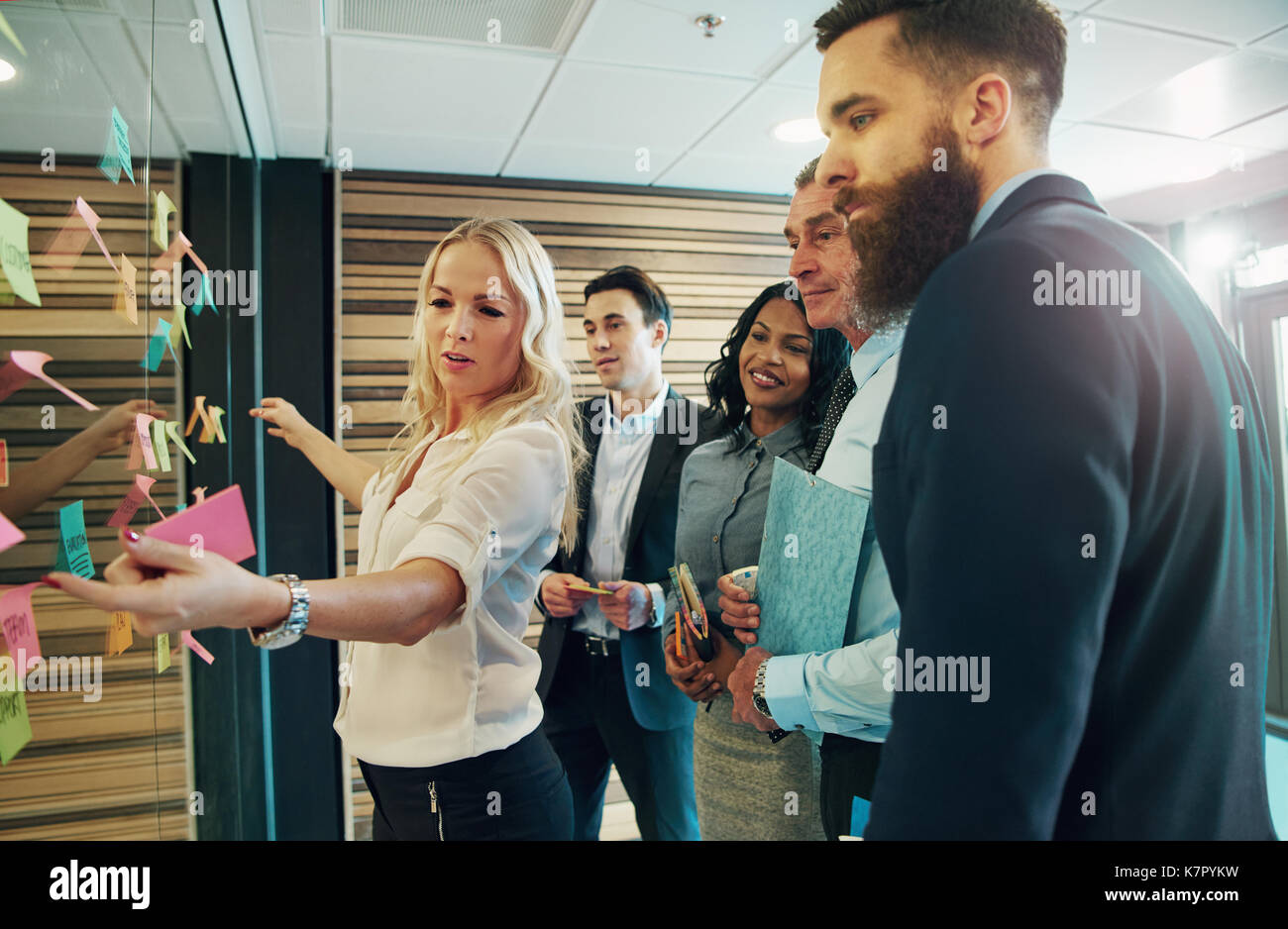Creative group of business people looking at sticky notes on glass partition in office Stock Photo