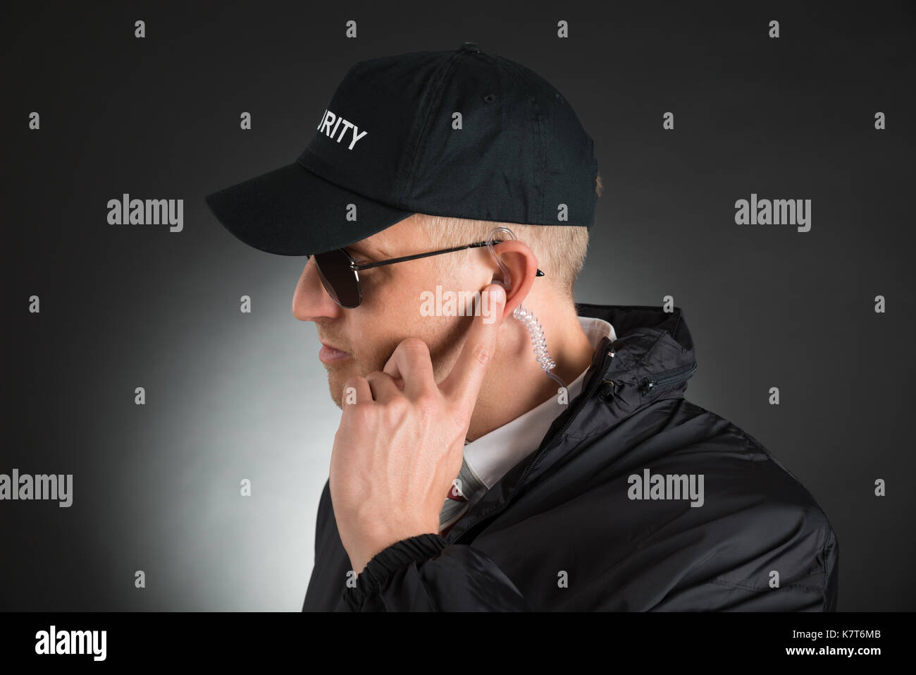 Secret Service Agent Listening To Earpiece Over Black Background Stock Photo