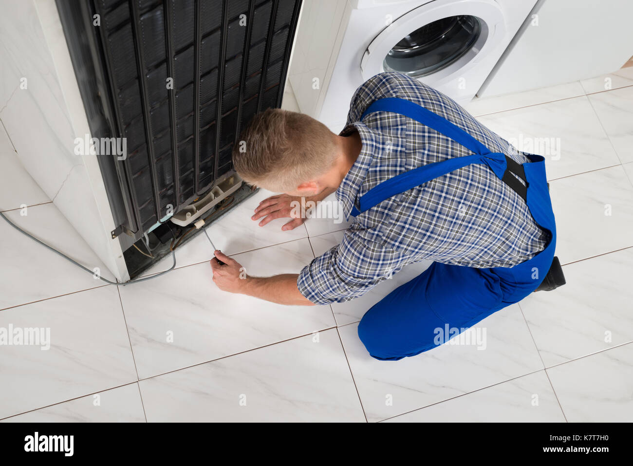 Young Male Repairman Making Refrigerator Appliance In Kitchen Room