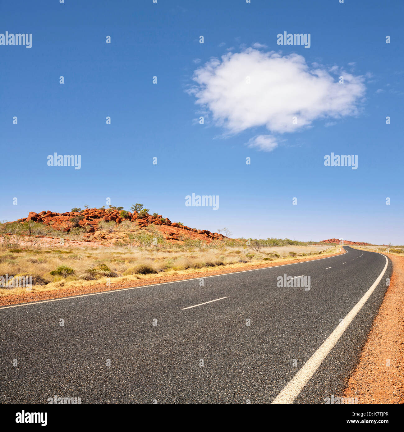 Long curving road stretching into the distance in the Pilbara region of Western Australia, under blue sky with single white cloud. Stock Photo