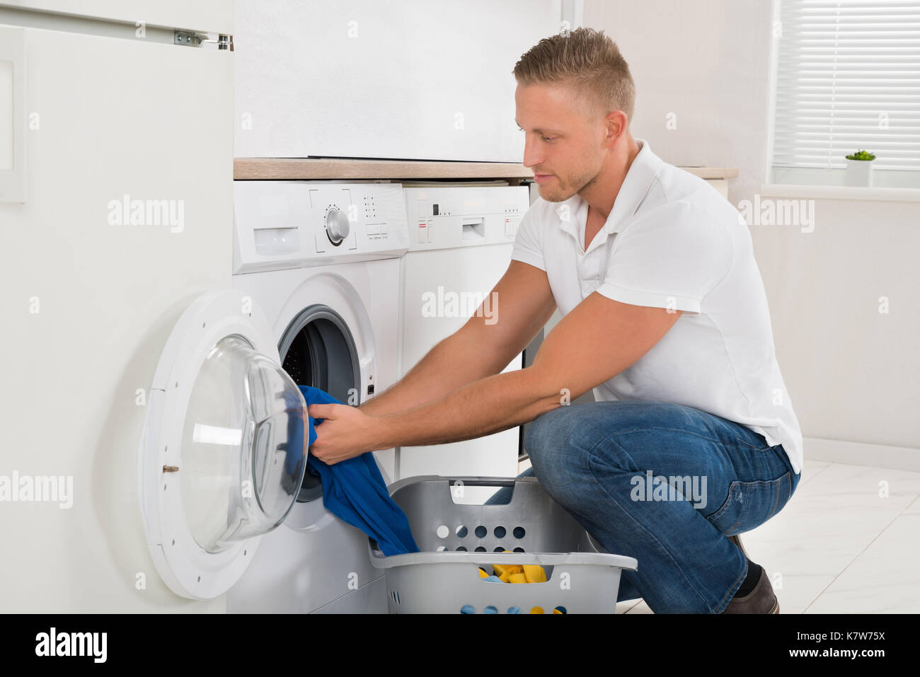 Man With Laundry Basket Loading Washing Machine With Clothes In Kitchen Room Stock Photo