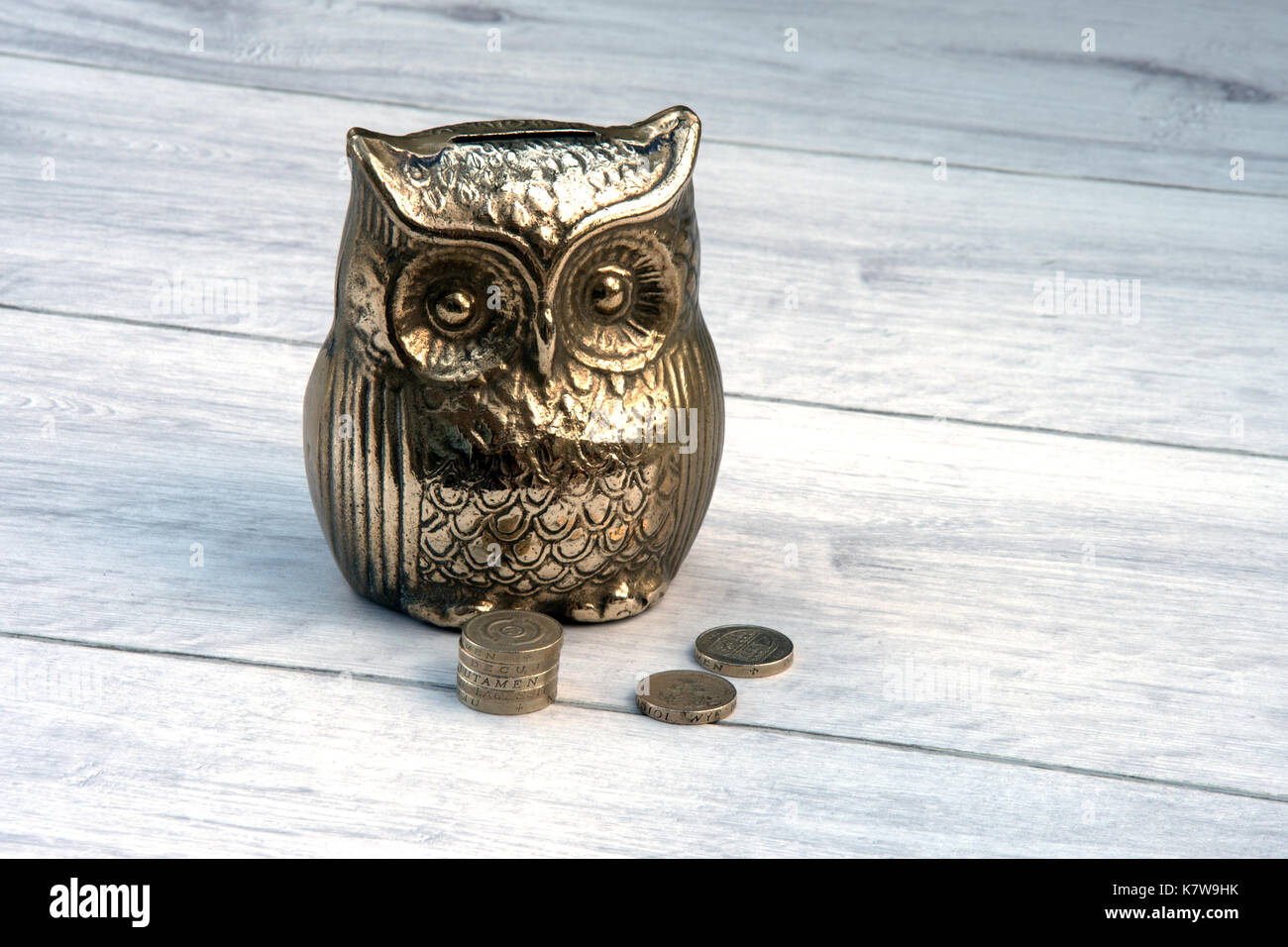 Brass owl money box with old one pound coins sterling. The UK one pound coin is being replaced and many are hiding away in money boxes. Stock Photo