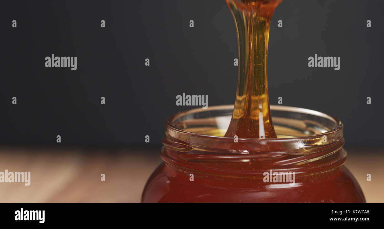 honey drips from dipper in glass jar Stock Photo