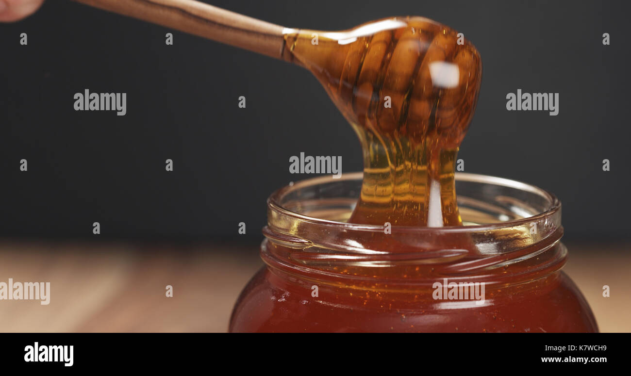 honey drips from dipper in glass jar Stock Photo