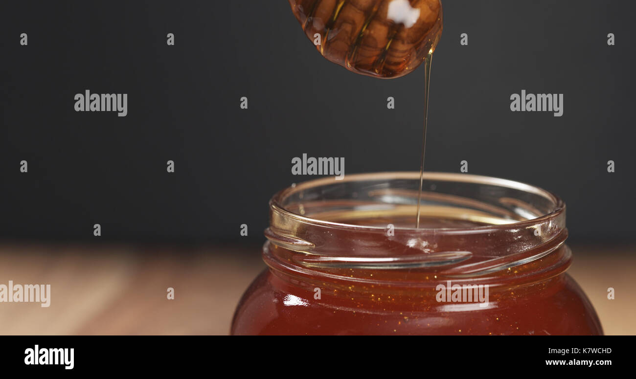 honey drips from dipper in glass jar Stock Photo
