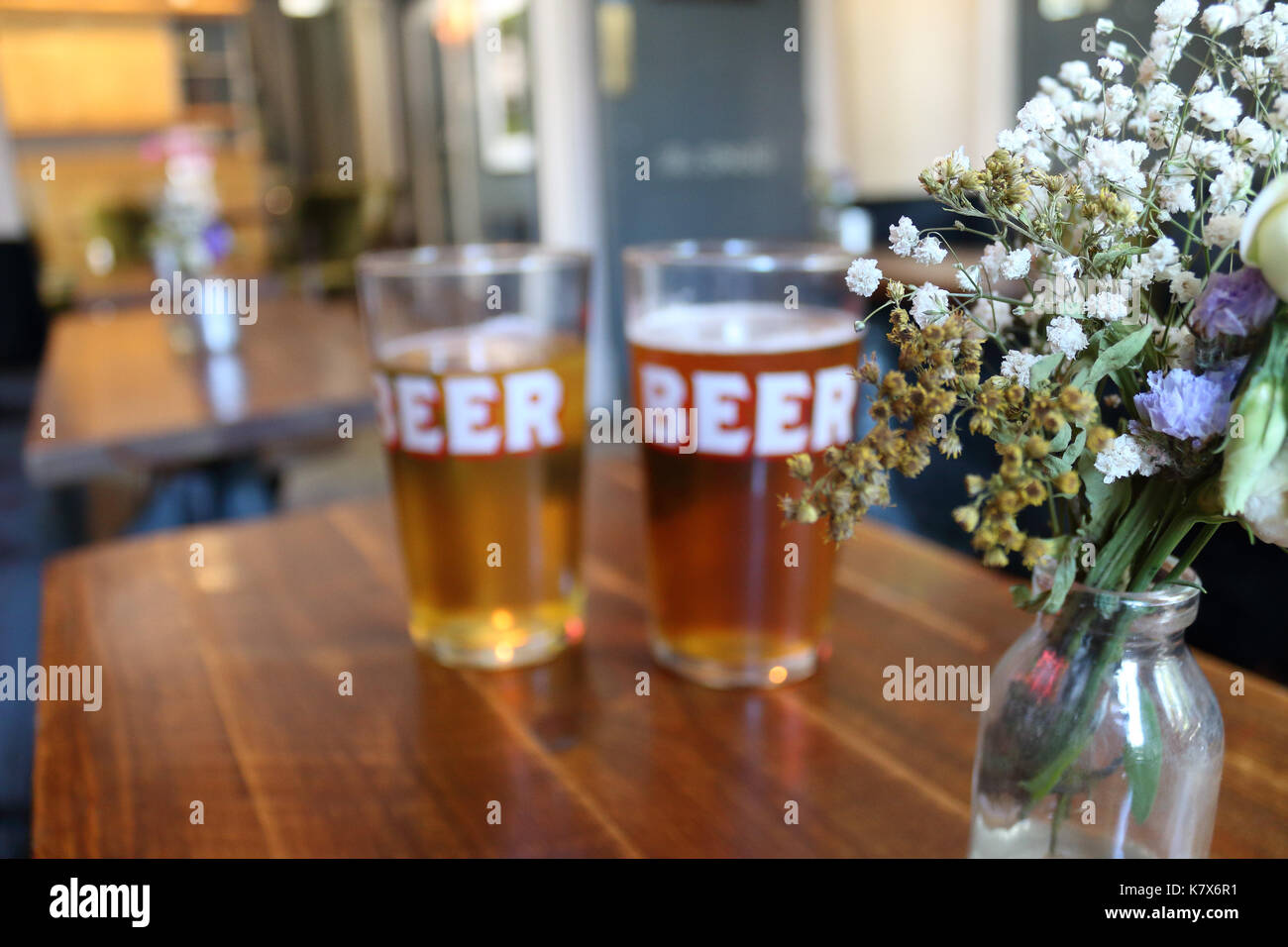 Two pints in 'BEER' glasses in a pub. Shallow focus on flower vase. London, UK. Stock Photo