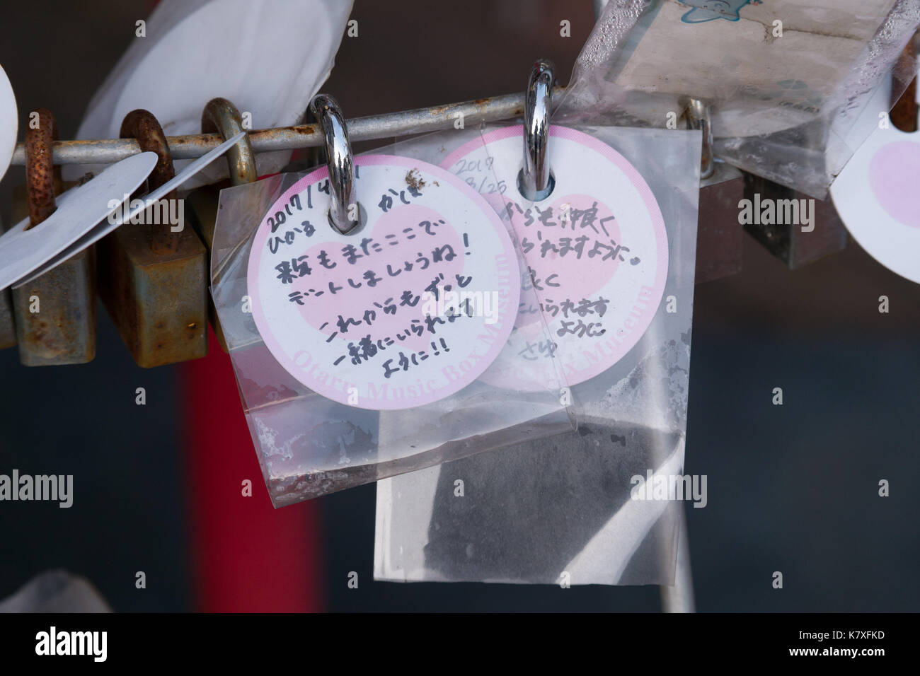 Small white and pink round note cards, attached to locks,  with pink heart in center with Japanese writing for wishes, good luck and love. Stock Photo