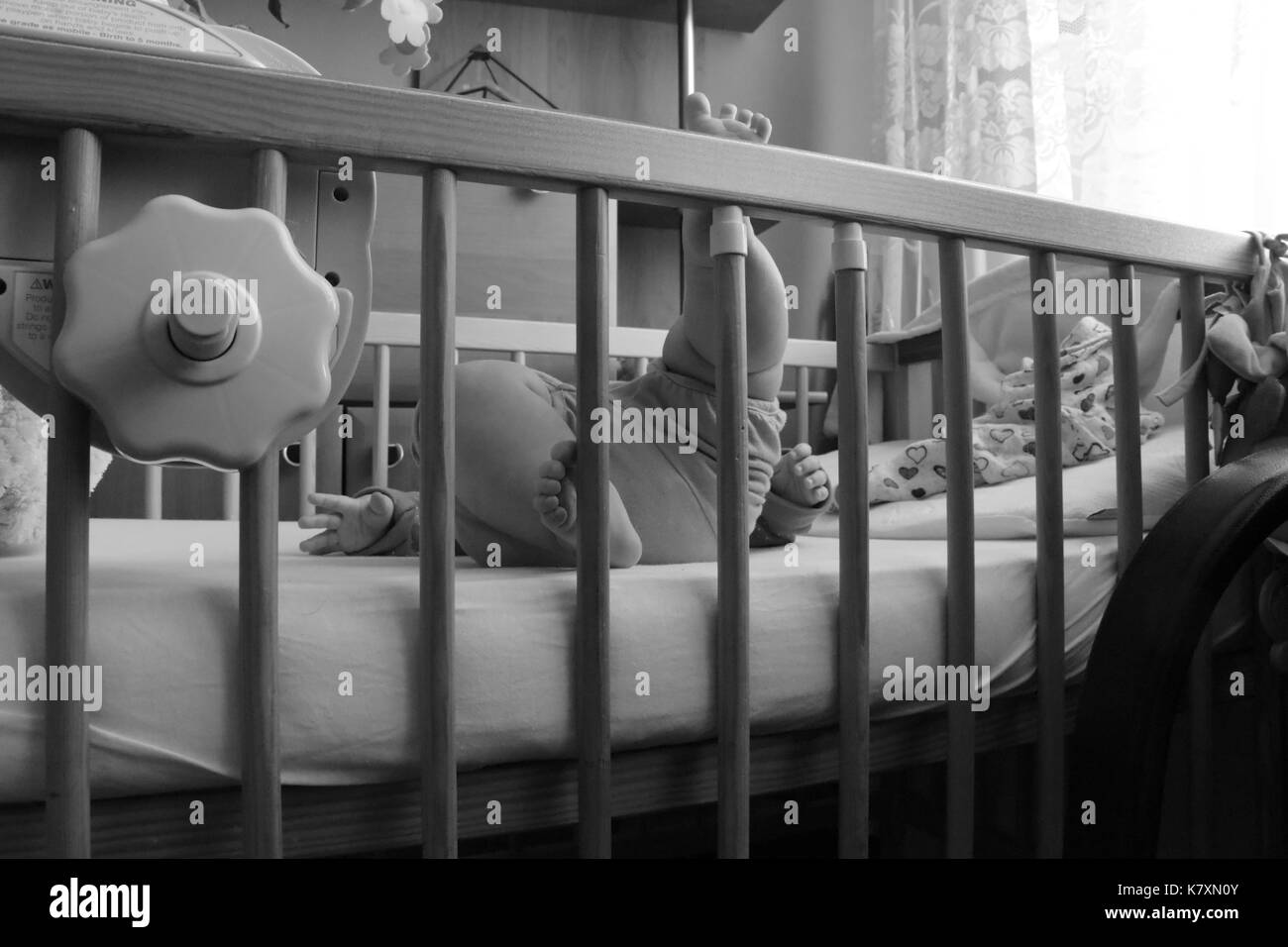 Baby, infant feet sticking out through the rails of a crib, cot, black