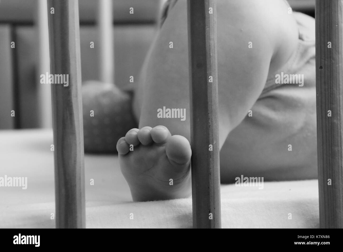 Baby, infant feet sticking out through the rails of a crib, cot, black and white photo