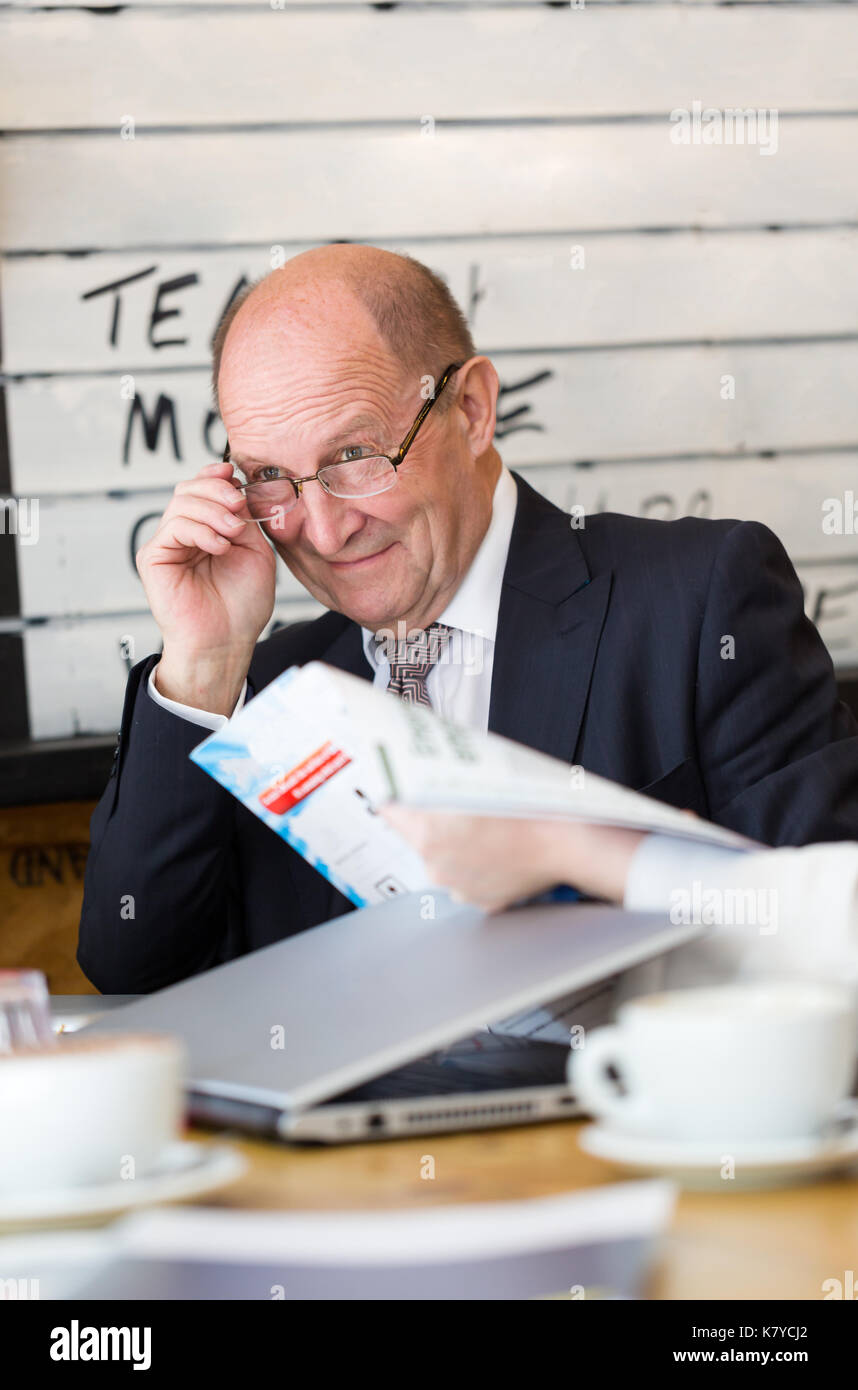 Senior manager, CEO, having conversation looks away keeps glasses in hand. Vertical portrait, candid shot Stock Photo