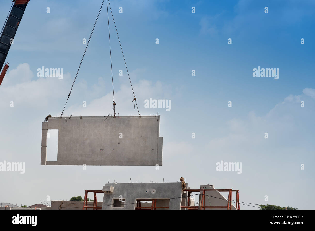 Construction site crane is lifting a precast concrete wall panel to