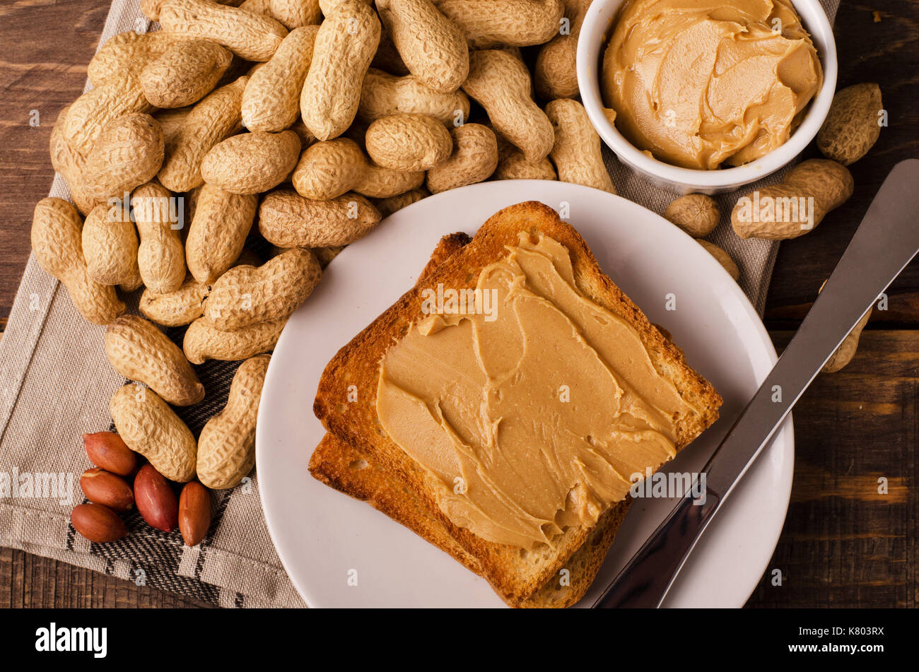 Portion of peanut butter sandwiches with peanuts in shel over black wooden background Stock