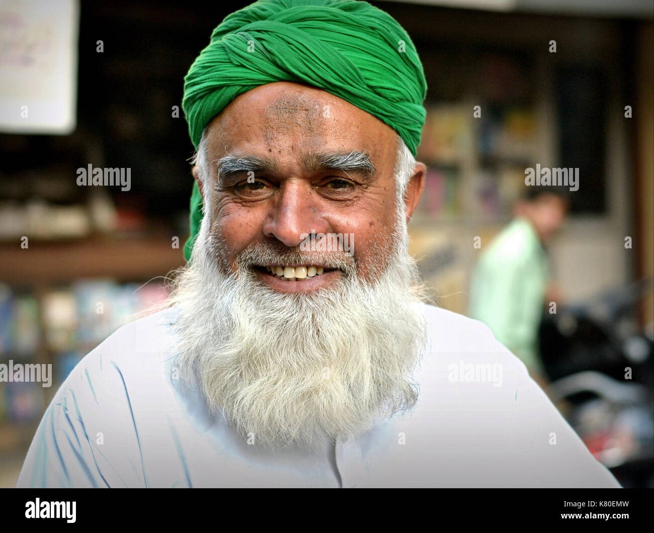 Elderly Indian Muslim man with white Muslim full-beard and prayer bump (zebibah) on his forehead wears a green turban and smiles for the camera. Stock Photo