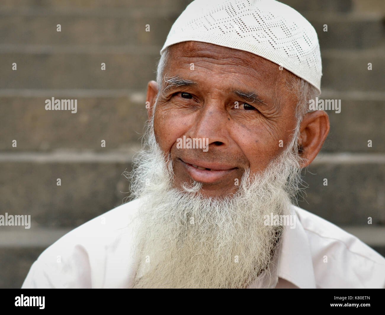 Elderly Indian Muslim man with Islamic beard wearing a white prayer cap (taqiyah) and poses for the camera. Stock Photo