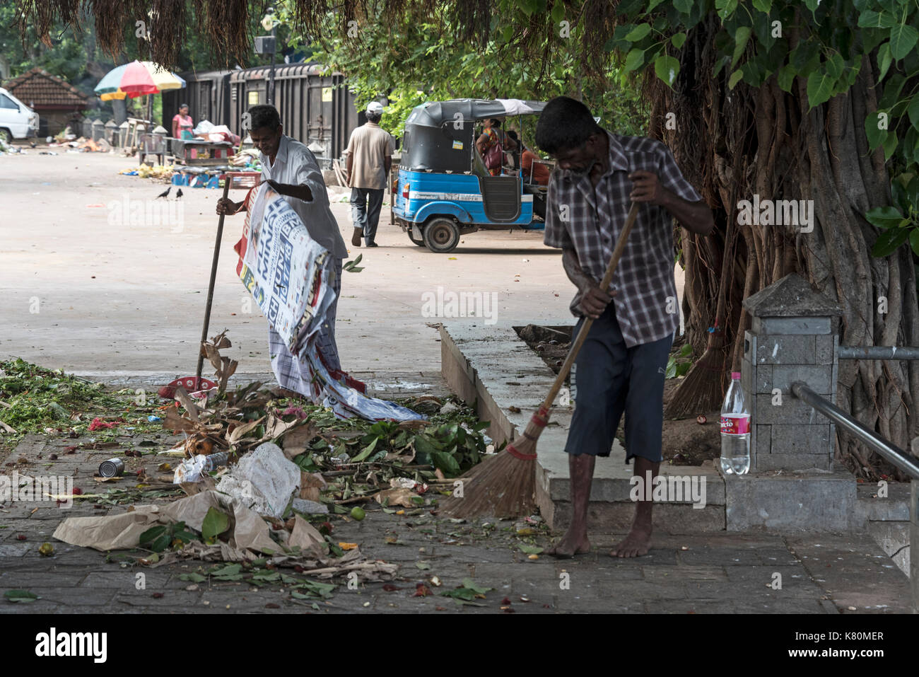 A couple of street cleaners clean up their rubbish (garbage) at a small