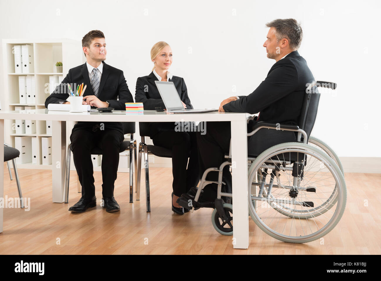 Mature Disabled Businessman Discussing With His Co-workers In Office Stock Photo