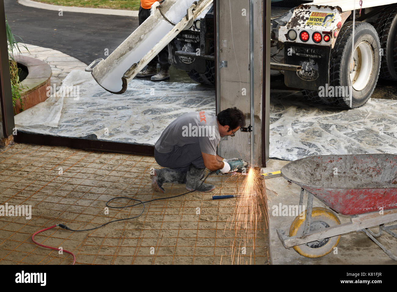 Worker grinding down steel garage door rails with sparks before pouring new concrete floor in residential garage Stock Photo