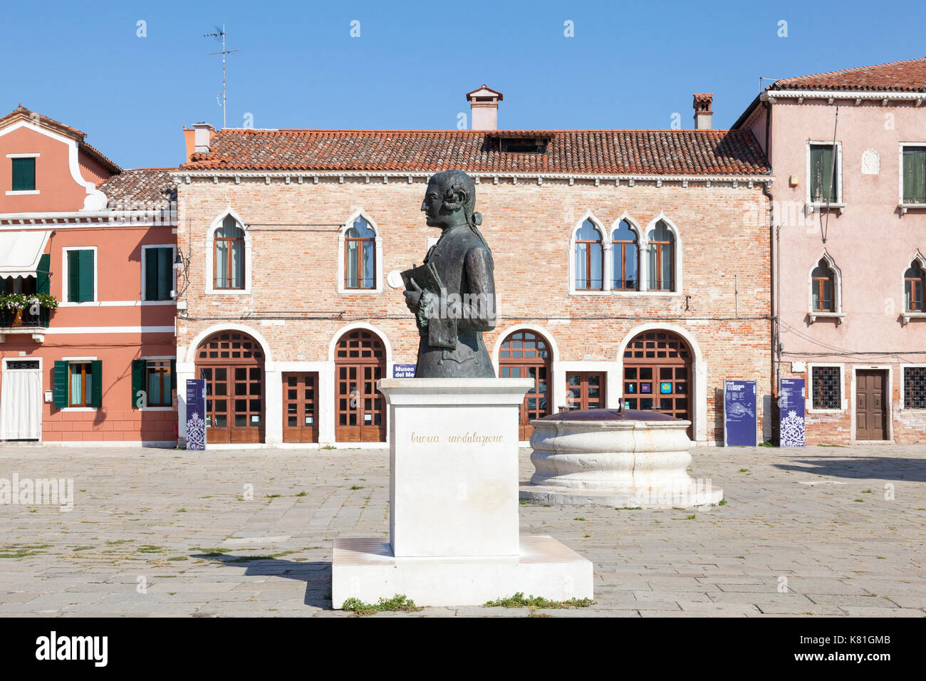 Statue of Baldassare Galuppi in Piazza Baldassare Galuppi, Burano, Venice, Veneto,  Italy, with the lace museum and ancient well head behind. Stock Photo