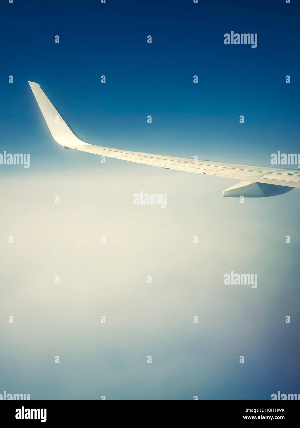 Wing of flying airplane above the clouds into an ethereal atmosphere Stock Photo