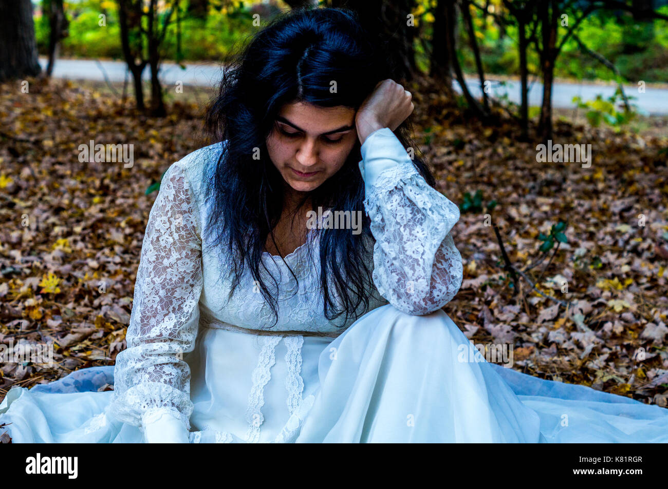 Young teen girl in dress laying on the ground outside looking down Stock Photo